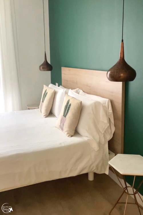 Photo shows a bed against a green wall with hanging lamps on either side. The bed is located in Sorrento Italy
