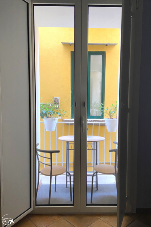 a set of glass doors is shown leading out to a small balcony with a bistro table and chairs in Sorrento Italy