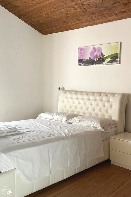 a bed with white sheets and a cream headboard is against a wall with a white nightstand in a loft apartment in Desenzano Italy
