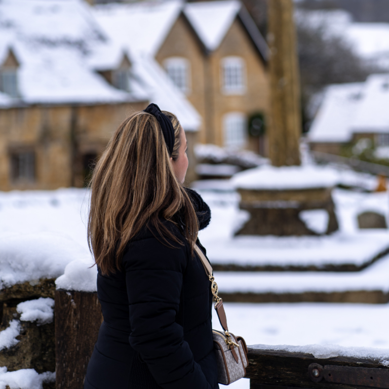 a woman is looking out over a small town covered in snow in the Cotswolds