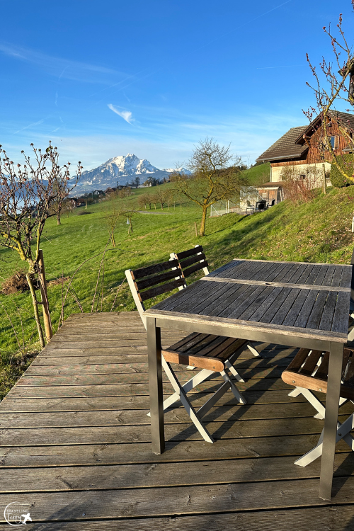 a wooden table and chairs on a deck patio overlooks green grass and a snow-capped Mt Pilatus from an Airbnb near Lucerne