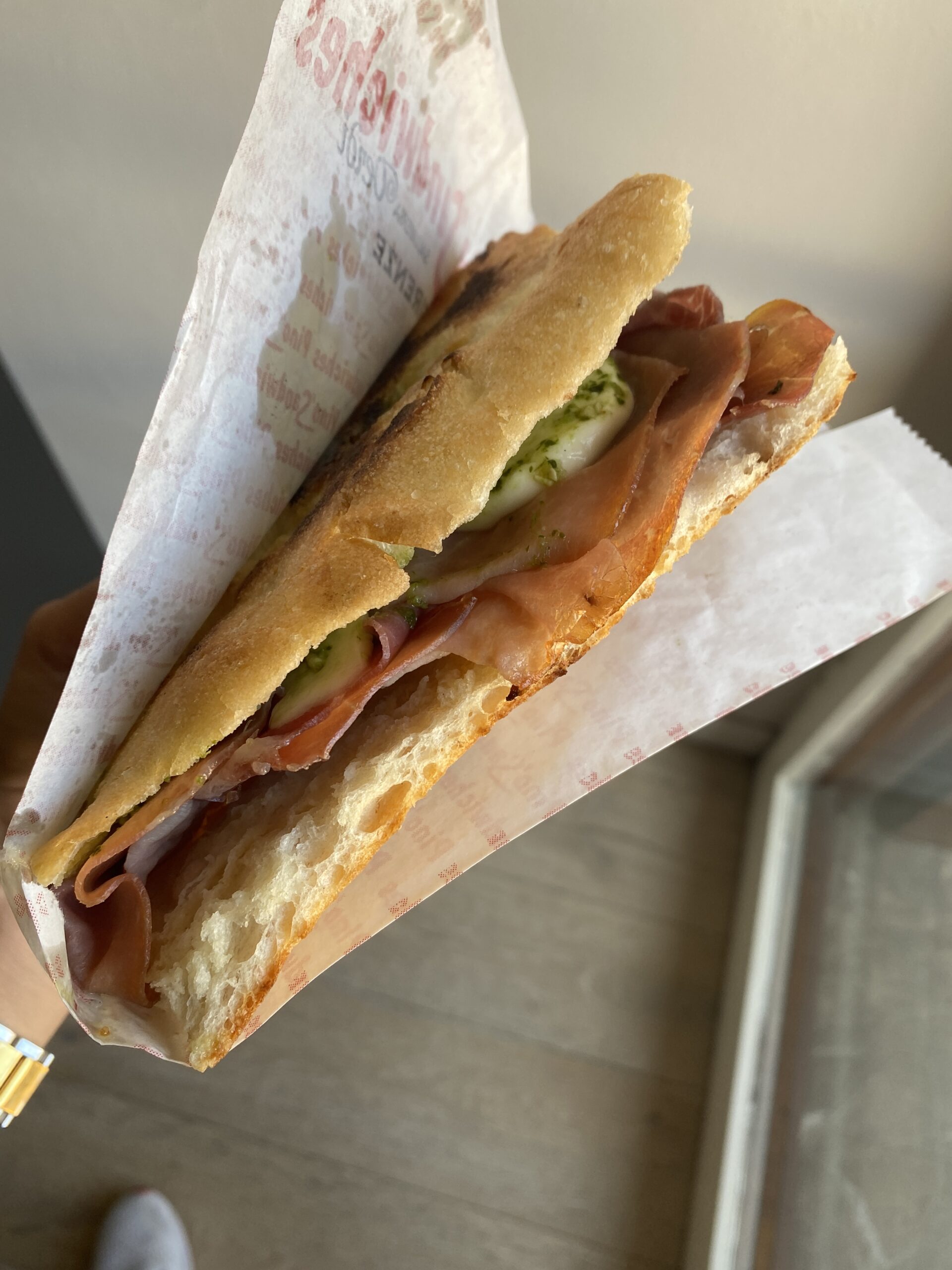 a sandwich with prosciutto, mozzarella, and pesto from Pino's in Florence is being held in the hands of a woman