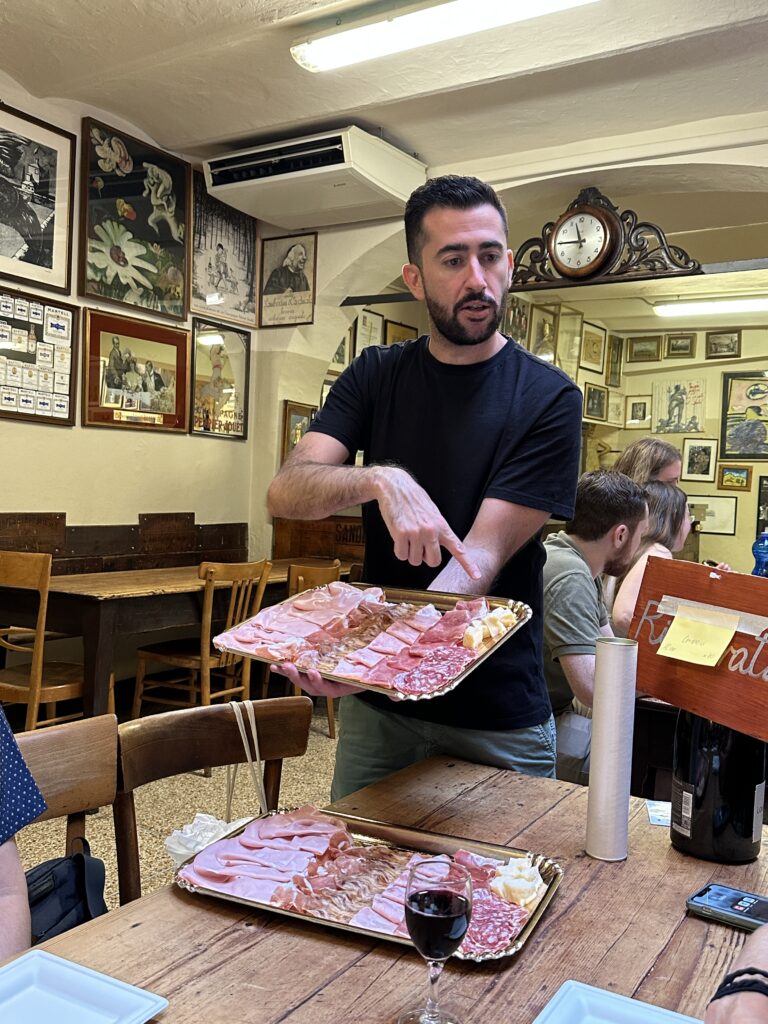 a man is holding a tray of Italian meats and cheeses.