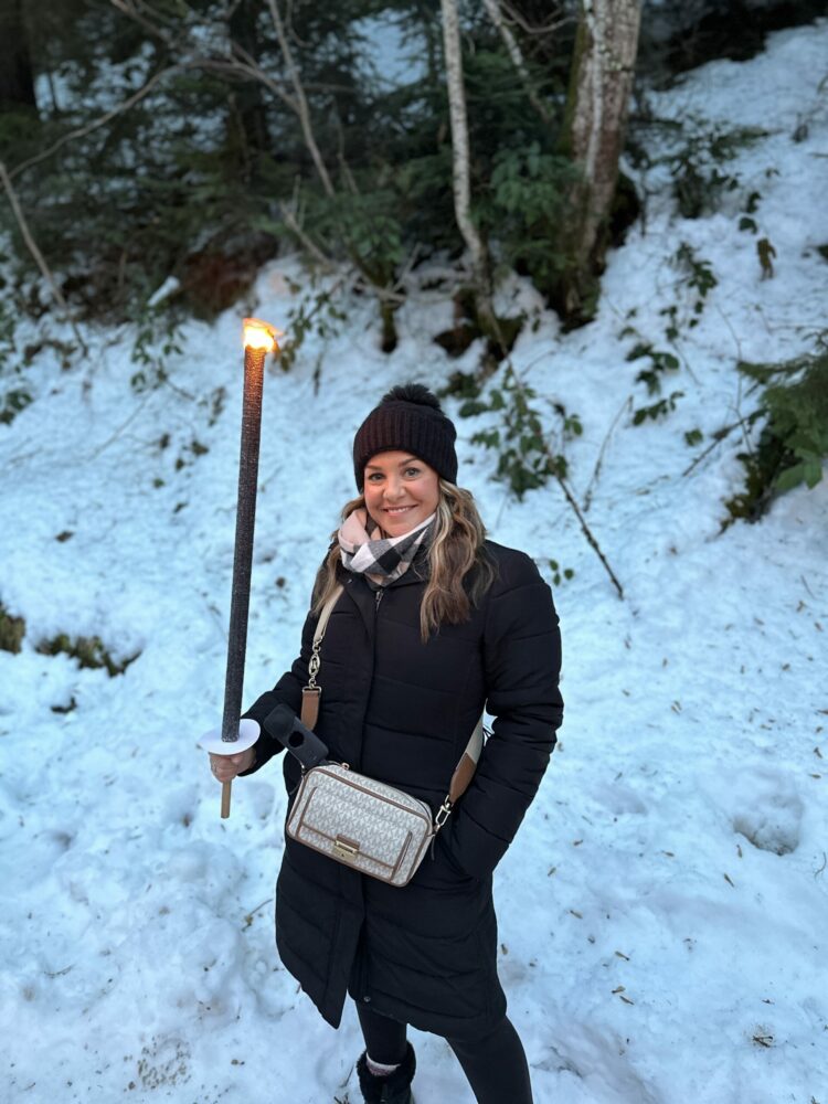 Ravenna Gorge Christmas Market 18 A woman warmly dressed in a black coat and beanie, holding a glowing torch while standing on a snowy path in the Black Forest near the Ravenna Gorge Christmas Market.