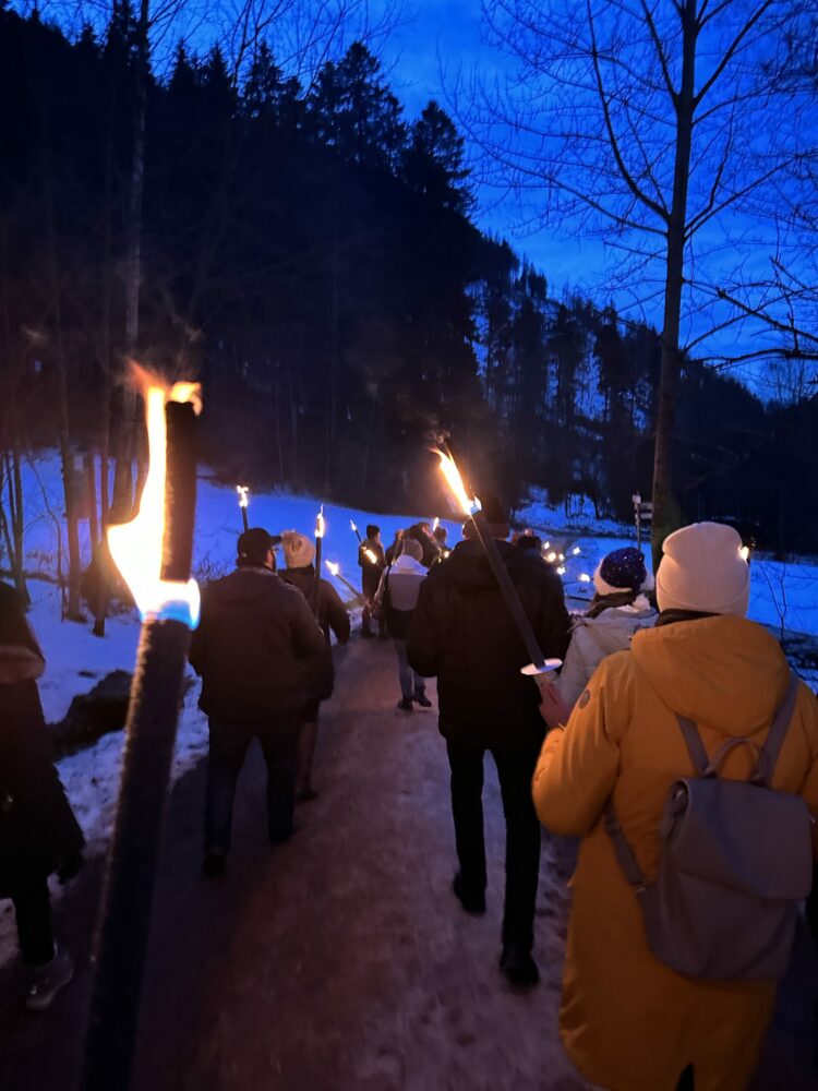 Ravenna Gorge Christmas Market 20 A group of visitors walking along a snowy forest path, illuminated by torches, during a magical evening near the Ravenna Gorge Christmas Market in the Black Forest, Germany.