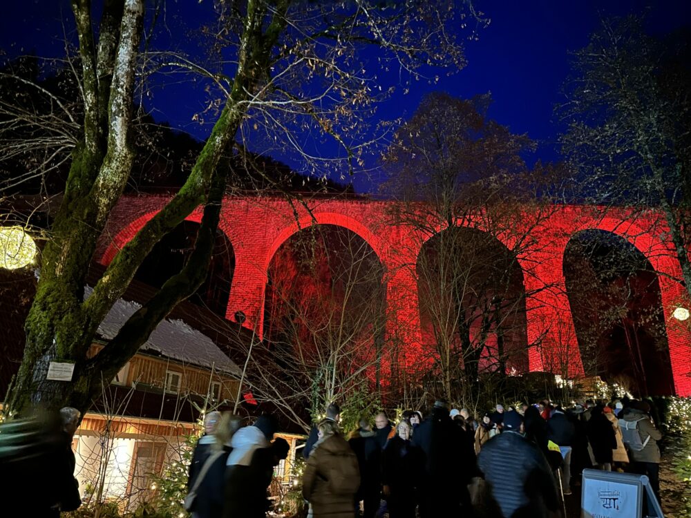 Ravenna Gorge Christmas Market 36 Crowds of visitors walking beneath the illuminated red arches of the Ravenna Viaduct at the Ravenna Gorge Christmas Market, surrounded by trees and festive decorations in the Black Forest, Germany.