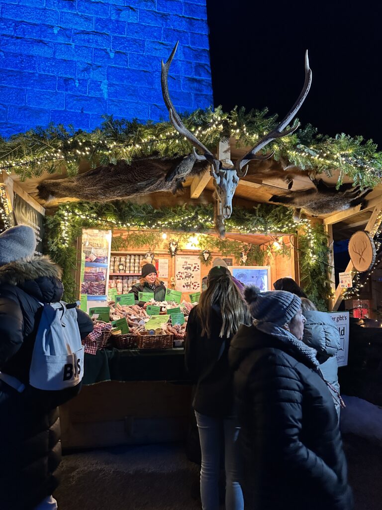 Ravenna Gorge Christmas Market 45 A decorated vendor stall at the Ravenna Gorge Christmas Market featuring rustic antlers, evergreen garlands, and a variety of local products for sale, illuminated by warm festive lighting.
