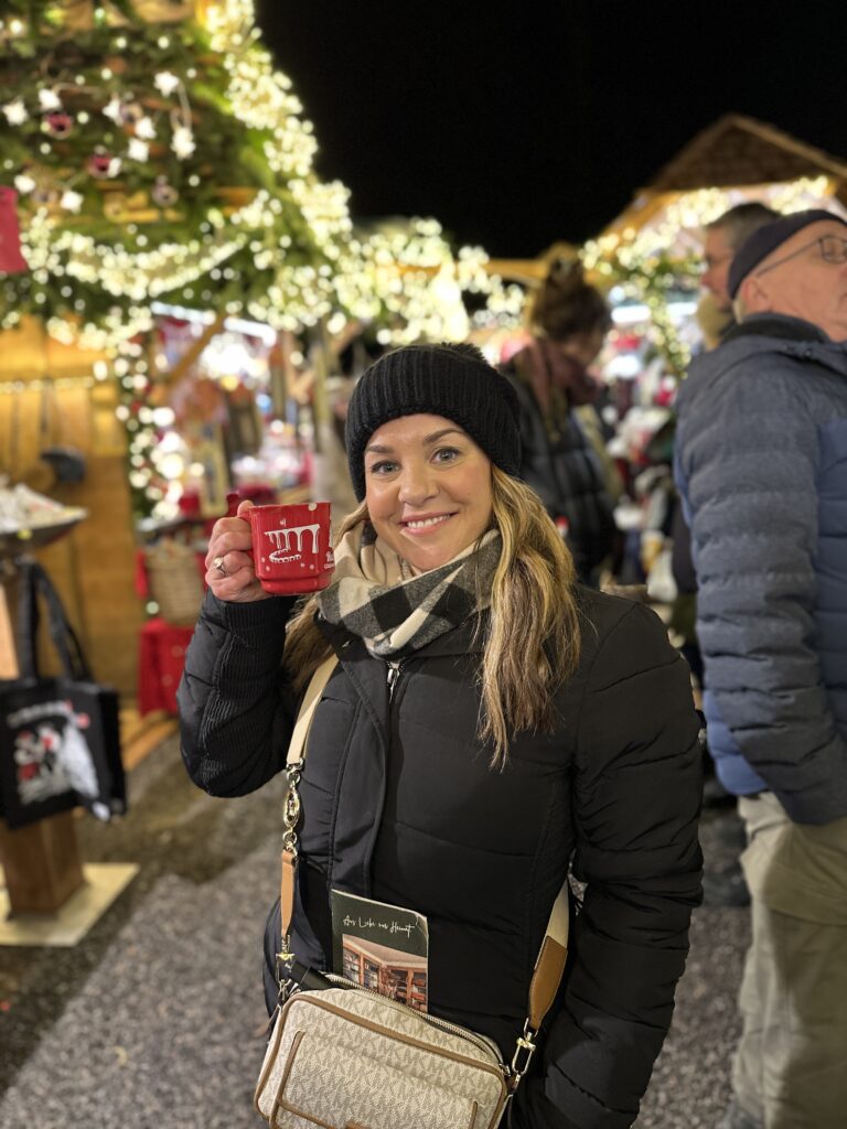 Ravenna Gorge Christmas Market 52 A woman smiling and holding a red Glühwein mug at the Ravenna Gorge Christmas Market, surrounded by twinkling lights and festive stalls.