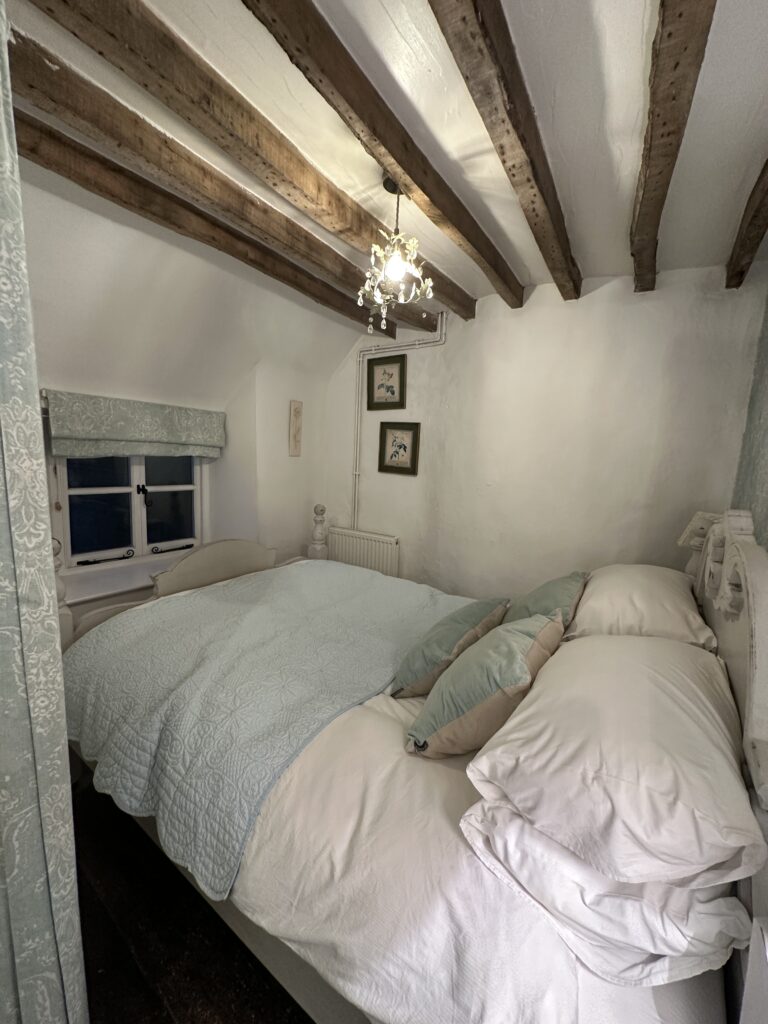 Chalford Cottage Cotswolds 10 Charming bedroom at Minnow Cottage featuring vintage-inspired decor, soft blue tones, and rustic wooden beams for an idyllic countryside ambiance