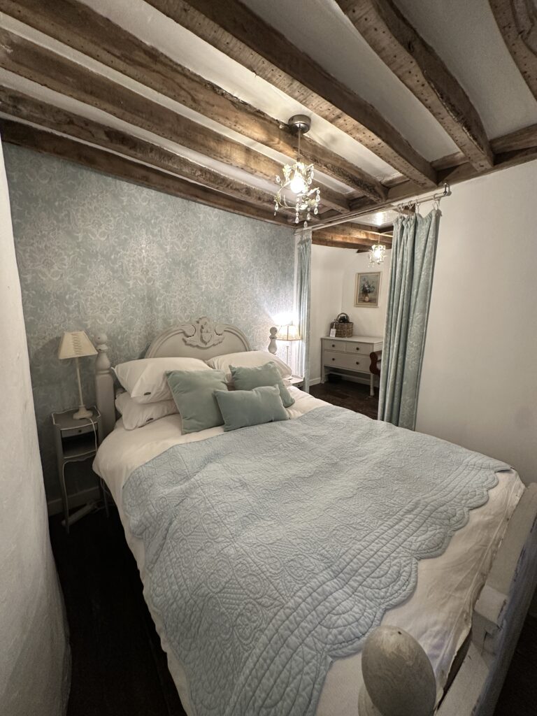 Chalford Cottage Cotswolds 11 Quaint bedroom at Minnow Cottage in the Cotswolds with exposed wooden beams, pastel bedding, and soft lighting for a relaxing, cozy retreat.