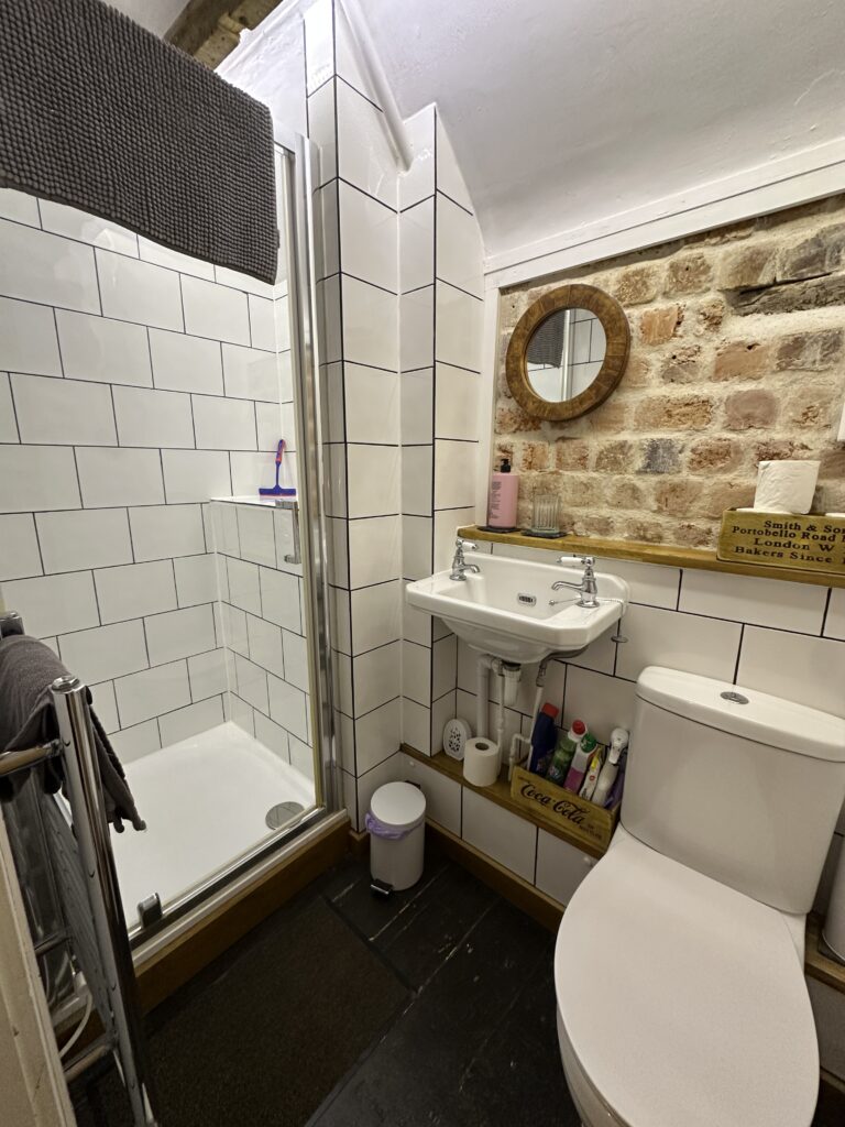 Chalford Cottage Cotswolds 13 Compact bathroom at Minnow Cottage with a walk-in shower, white subway tiles, and exposed stonework for a charming, rustic-modern feel.