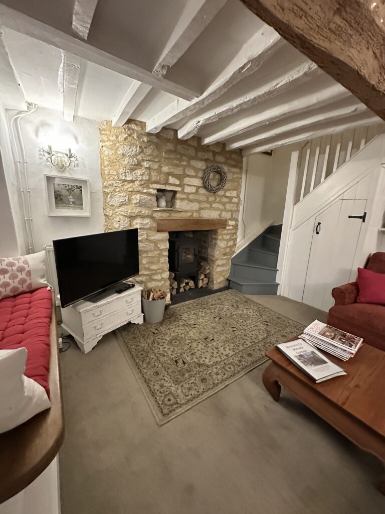 Chalford Cottage Cotswolds 15 Cozy living room at Minnow Cottage in the Cotswolds, featuring a rustic stone fireplace, exposed beams, and comfortable seating for a warm countryside retreat.