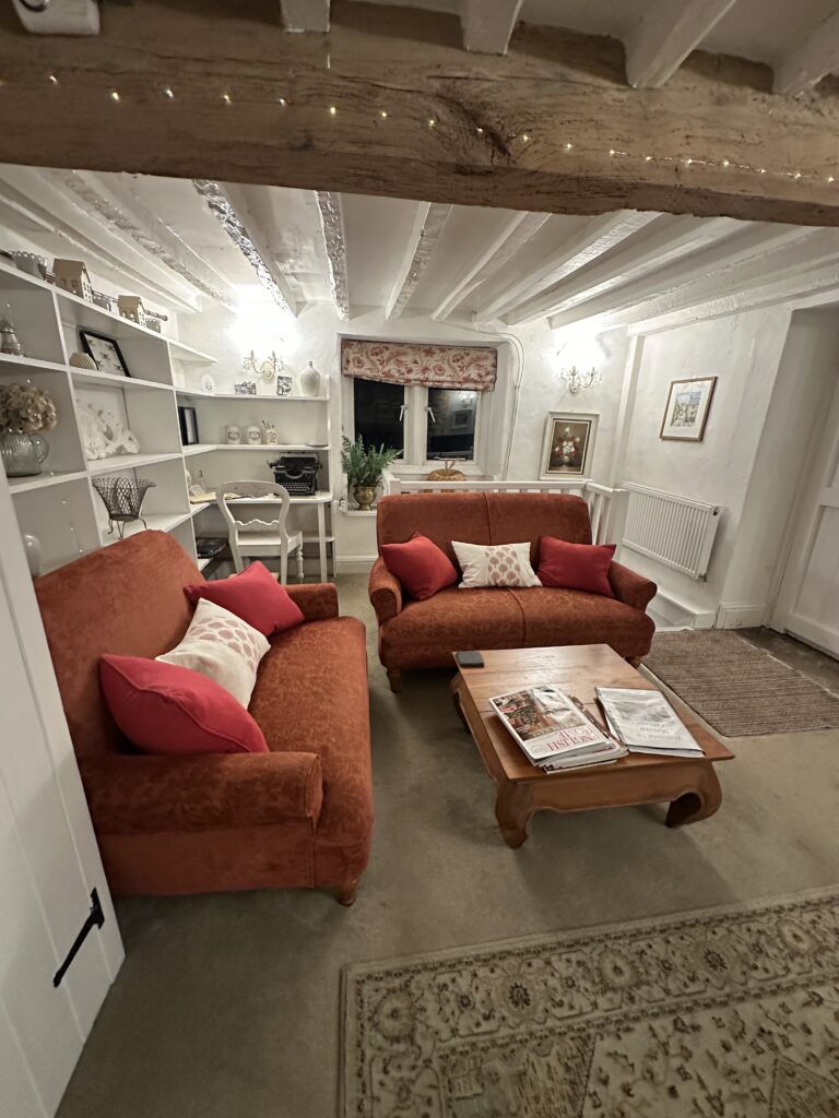Chalford Cottage Cotswolds 16 Comfortable living room at Minnow Cottage featuring red sofas, a wooden coffee table, and a window seat, exuding charm and warmth for a countryside escape.