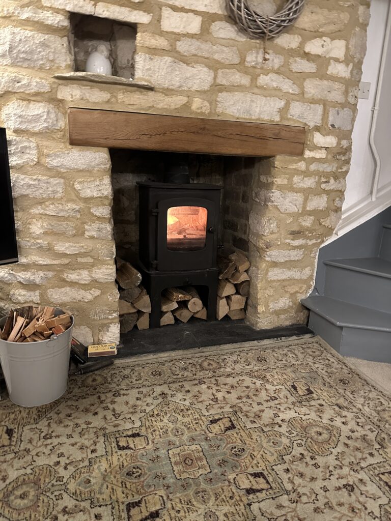 Chalford Cottage Cotswolds 19 Inviting living room at Minnow Cottage with a stone fireplace, wood-burning stove, and cozy seating, ideal for relaxing evenings in the Cotswolds.