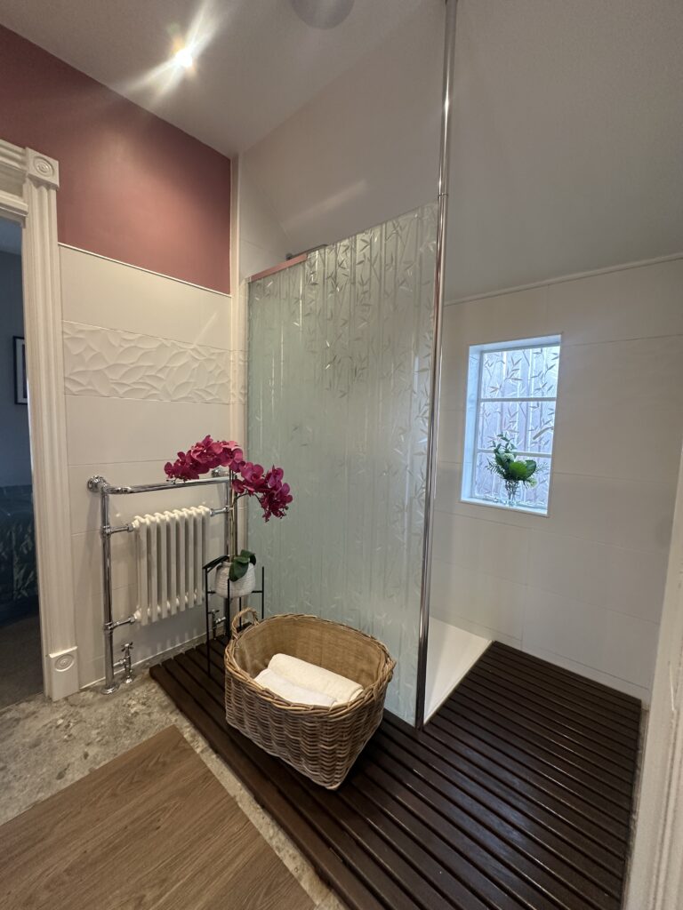 Stratford Upon Avon Penthouse 3 Modern bathroom in a Stratford-Upon-Avon penthouse, showcasing a glass-enclosed shower, wicker storage basket, and fresh orchid decor.