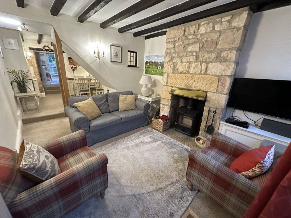 Inviting Cotswold living room at Lane’s Cottage with wood-burning stove, checkered armchairs, and traditional front door.