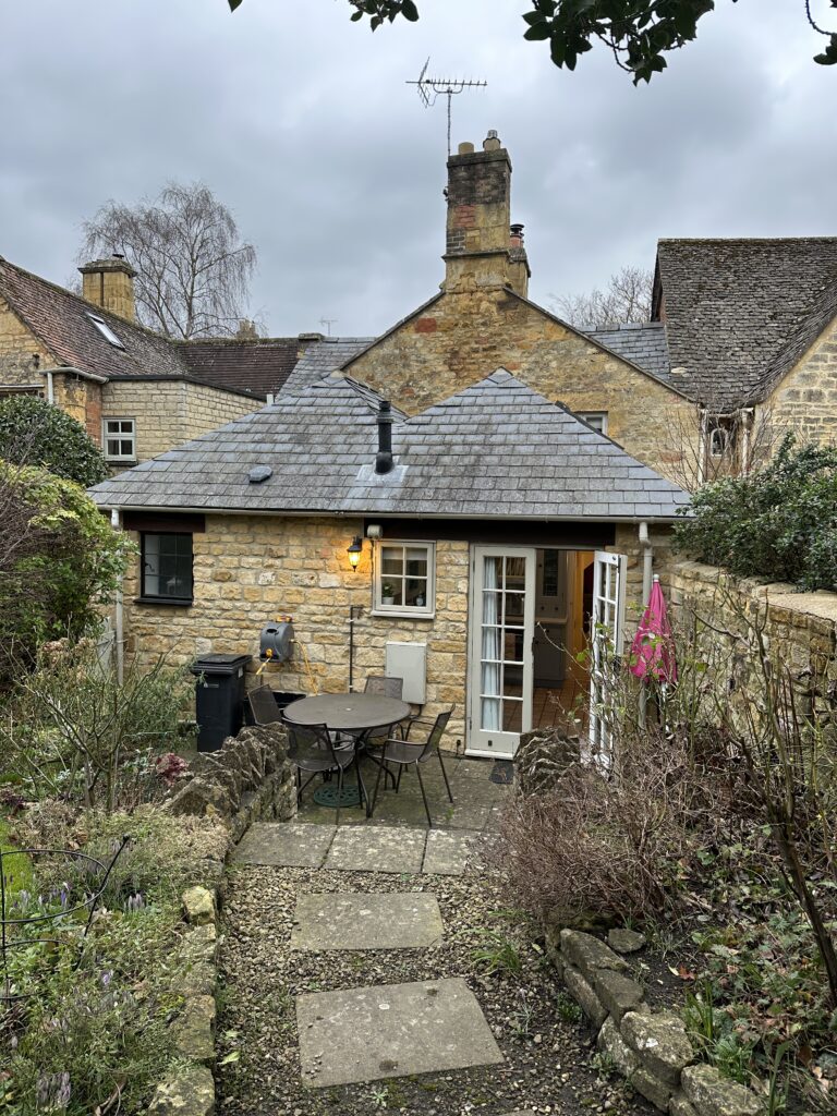Charming back patio of Lane’s Cottage with bistro table and view of the cottage’s Cotswold stone walls.
