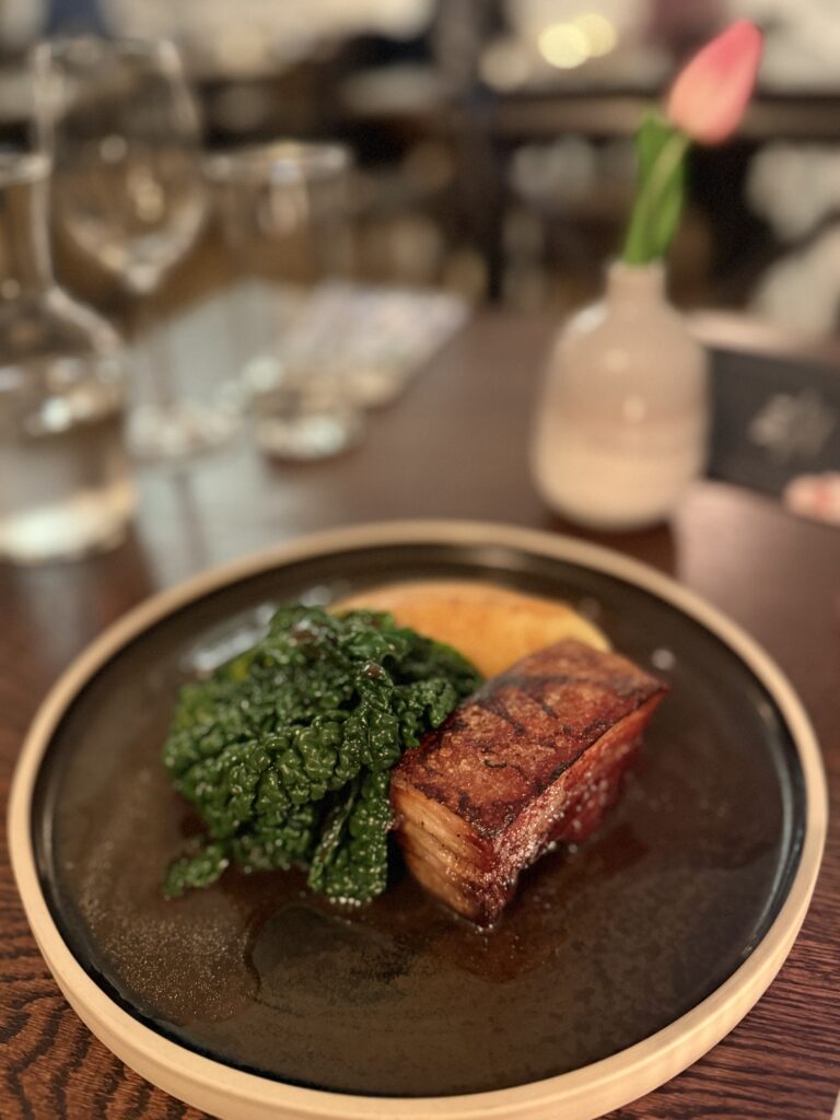 IMG_8222 Crispy pork belly with a golden crust served with greens and puree on a plate at a restaurant in England