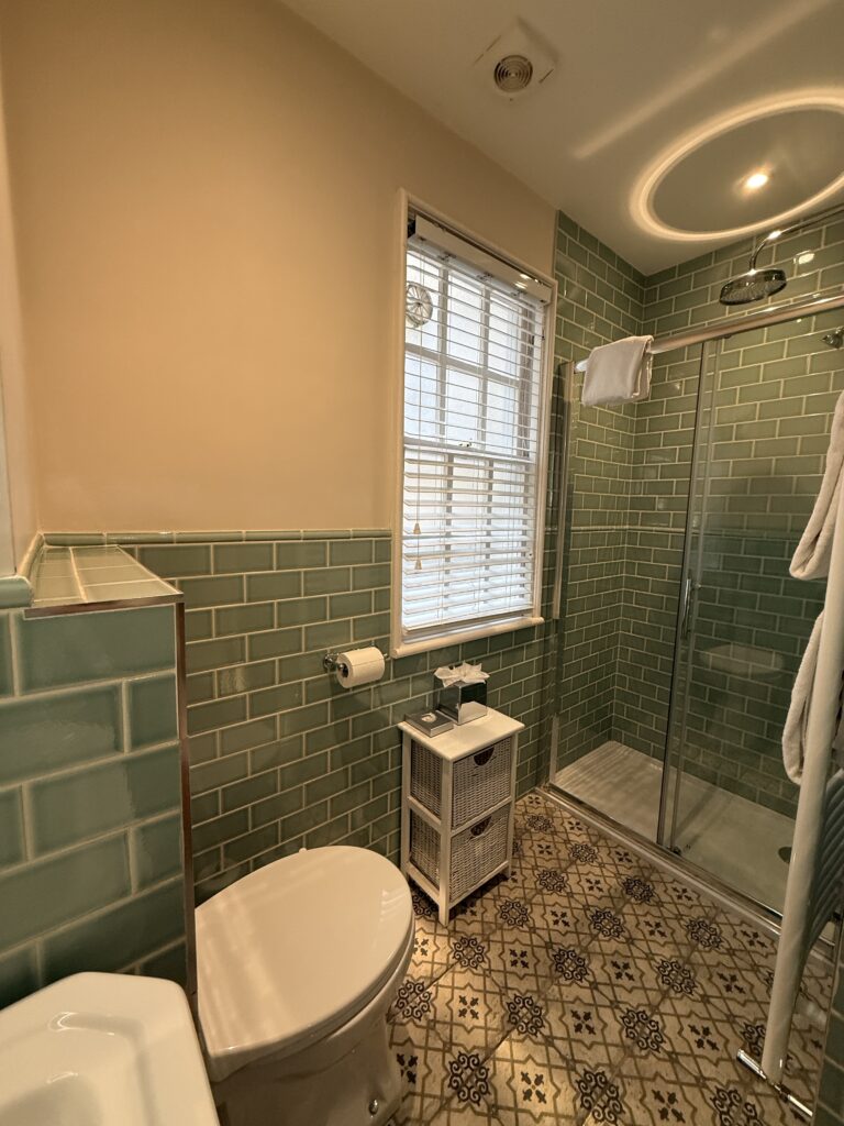 Ensuite bathroom at Eight Hotel Bath with sage green metro tiles, patterned floor tiles, glass shower enclosure, and white towels