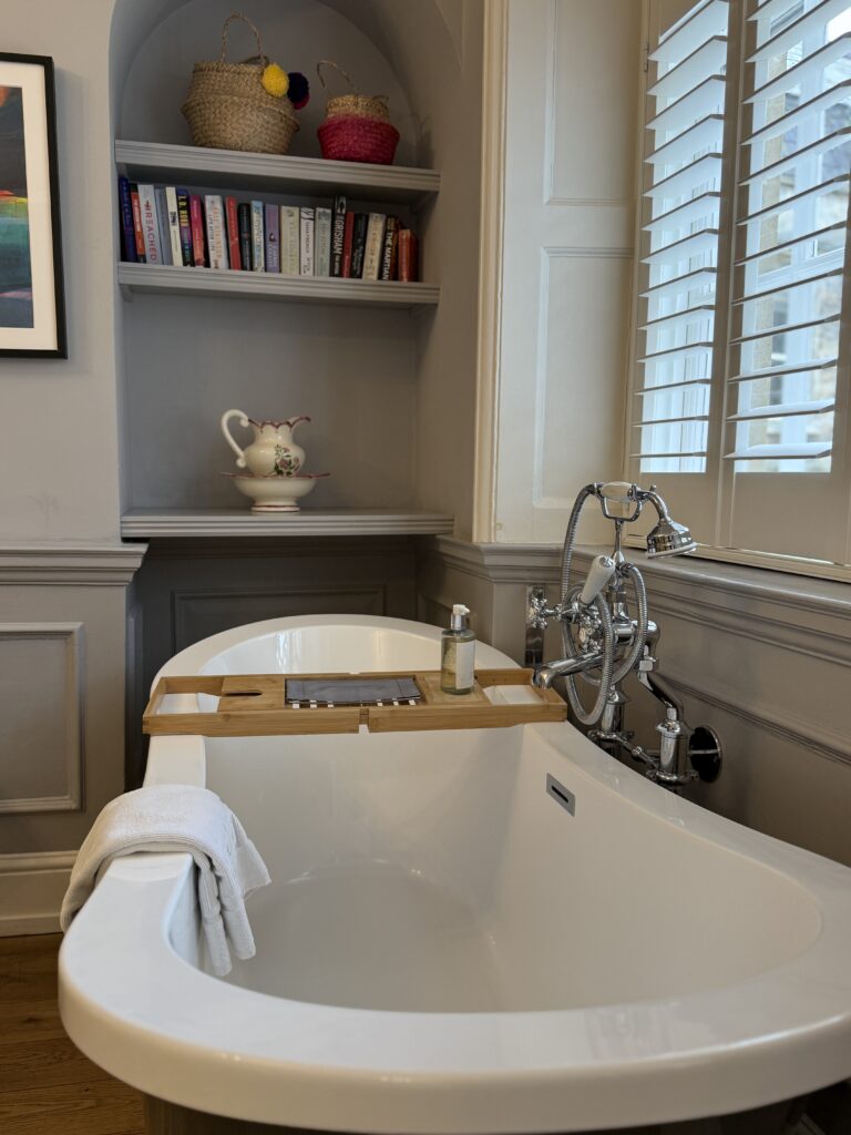 Freestanding bathtub with chrome taps and a bamboo bath caddy at Eight Hotel Bath, with built-in bookshelves and Georgian panelled walls in the background